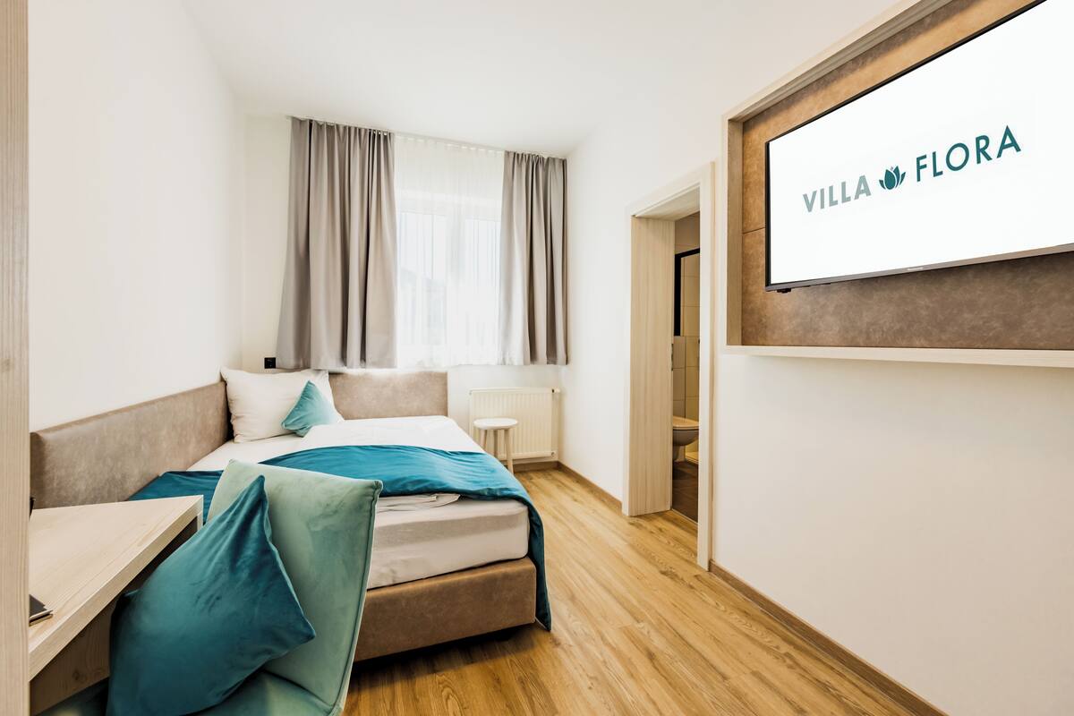 Een hotelkamer met een bed, een bureau, een aan de muur bevestigde televisie en een raam met gordijnen.