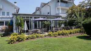 A building with outdoor seating and a garden area. - Hotel Villa Flora (Velden am Wörther See)