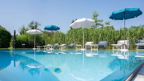 A swimming pool with lounge chairs and umbrellas. - Hotel Villa Flora (Velden am Wörther See)
