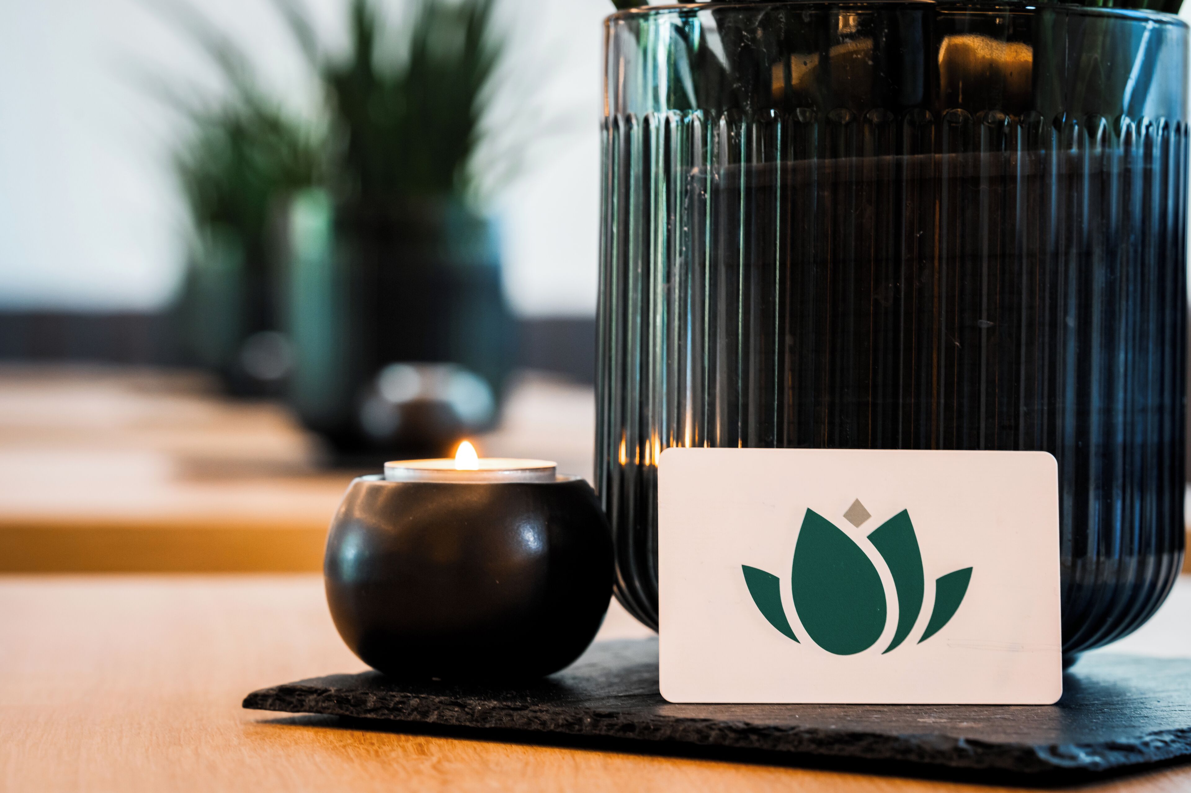 A candle in a glass holder, a card with a green lotus symbol, and a blurred background with greenery.