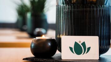 A candle in a glass holder, a card with a green lotus symbol, and a blurred background with greenery.