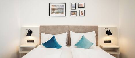 Une chambre d’hôtel avec un lit, deux tables de chevet, une petite table et un mur orné de tableaux.
