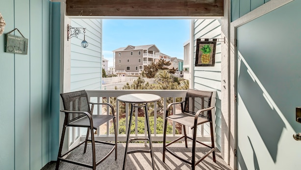 A balcony with two chairs and a table, overlooking a building with a pineapple decoration. - Beach, Please! (Carolina Beach)