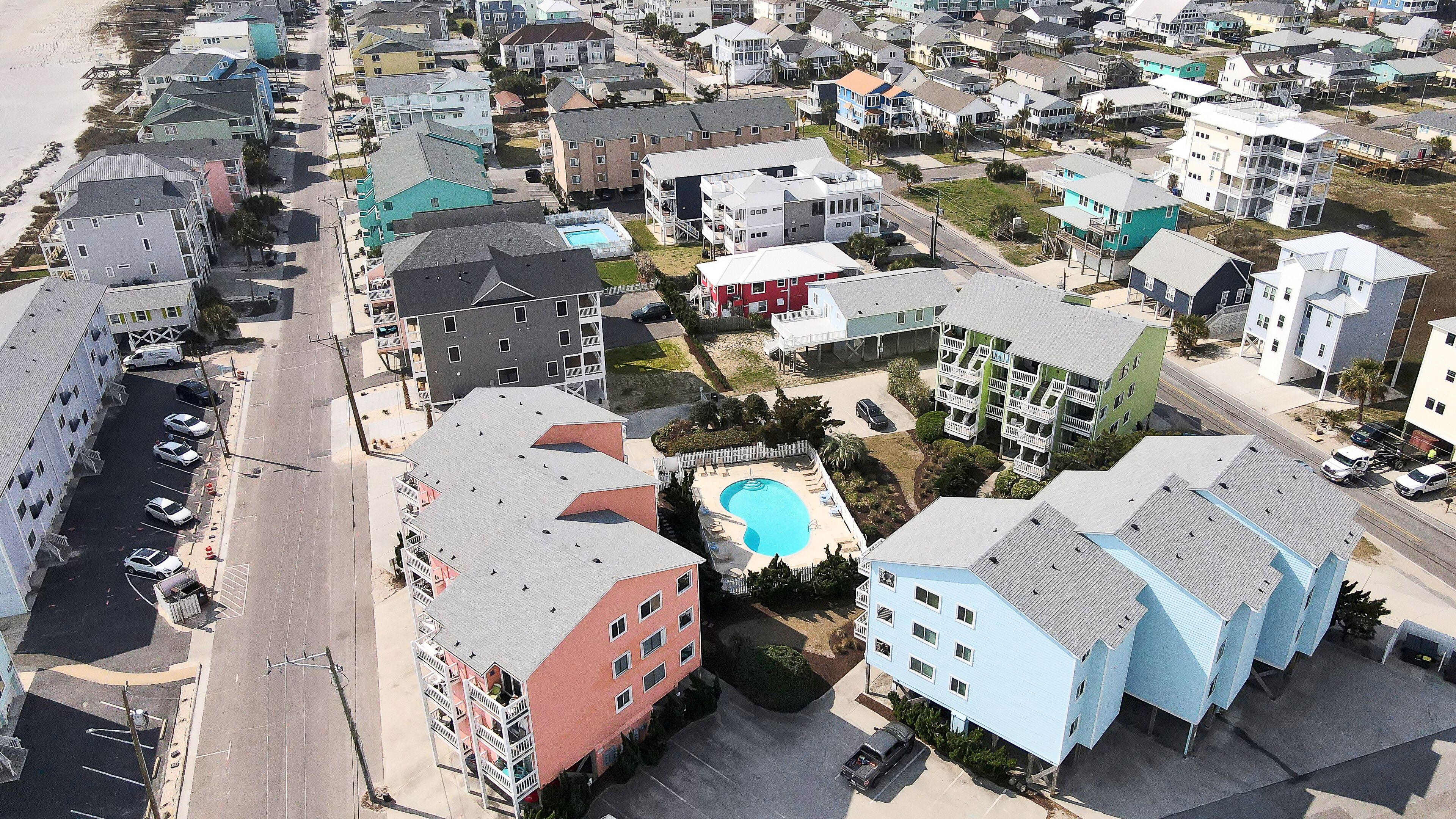 Vista aérea de una zona residencial con varios edificios de varios pisos, una piscina y una playa al fondo.