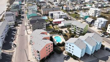 Vista aérea de una zona residencial con varios edificios de varios pisos, una piscina y una playa al fondo.