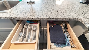 A kitchen with a granite countertop, a stainless steel sink, and a drawer containing utensils and a quilted cloth. - Beach, Please! (Carolina Beach)