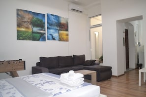 Relax in a serene space with a large bed, sofa, and artwork, surrounded by natural light and a wooden floor.