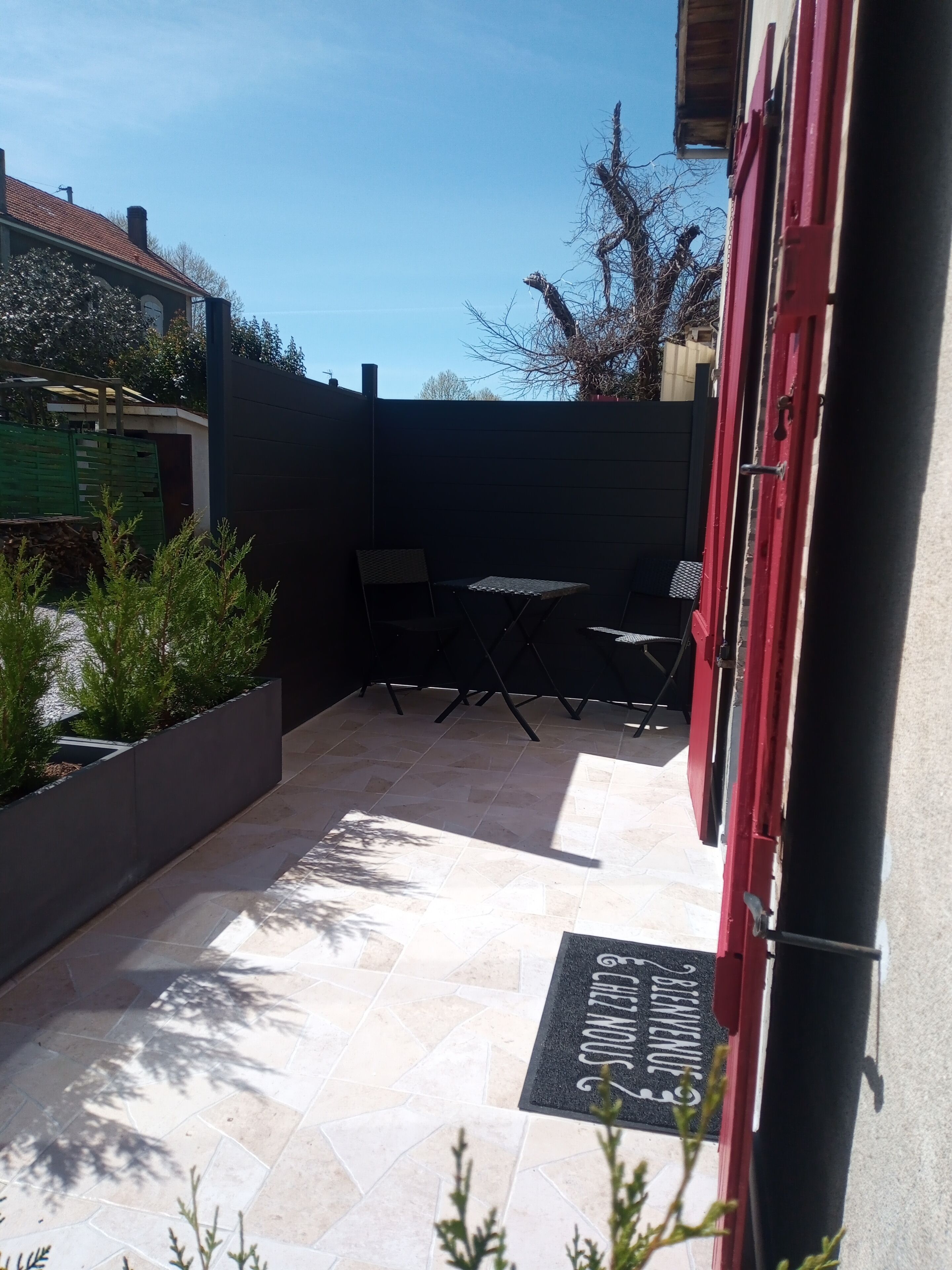 Un espace extérieur aménagé en patio, avec un sol carrelé, une clôture en métal noir et une porte rouge.