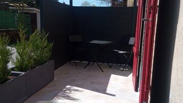 Un espace extérieur aménagé en patio, avec un sol carrelé, une clôture en métal noir et une porte rouge.