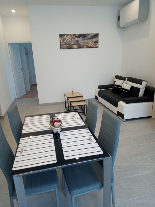 A modern living room with a dining area, featuring a sofa, a coffee table, and a painting on the wall.