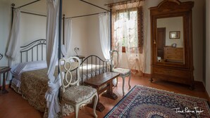 Ein Schlafzimmer mit einem Himmelbett, einem hölzernen Schminktisch, einem Sessel und einem kleinen Tisch.