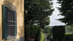 Ein Innenhof mit einem gelben Gebäude, einem großen Baum und einer Hecke.