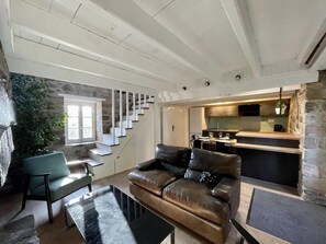 A modern living room with a leather sofa, a dining area, a kitchen, and a staircase with a stone wall. - La Cidrerie du port (landevennec)