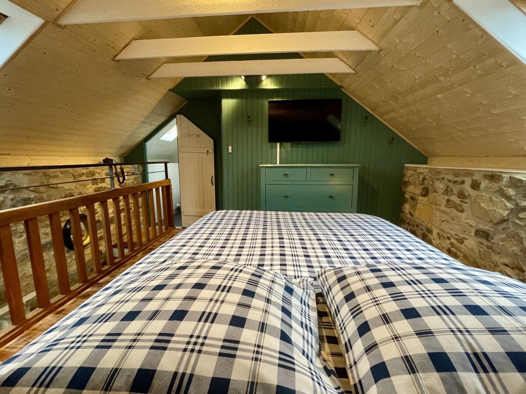 Un dormitorio con techo inclinado, una cama de madera, un aparador y un televisor montado en la pared.