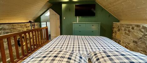 Un dormitorio con techo inclinado, una cama de madera, un aparador y un televisor montado en la pared.