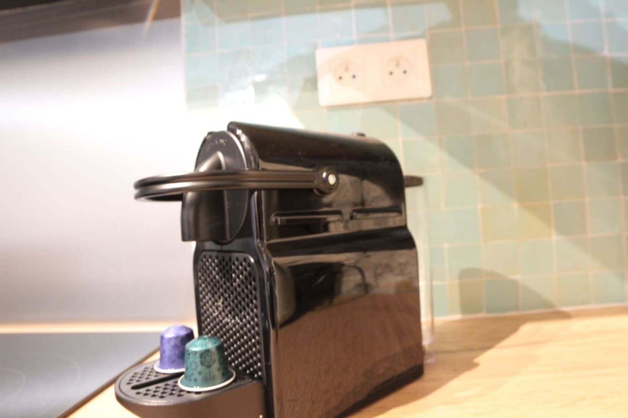 A kitchen with a toaster on the counter, a power outlet on the wall, and a tiled backsplash.
