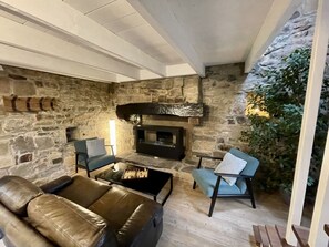A stone-walled room with a fireplace, leather sofa, and a blue armchair. - La Cidrerie du port (landevennec)