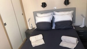 A neatly made bed with two pillows, a bedside table with a lamp, and a wall-mounted light fixture.