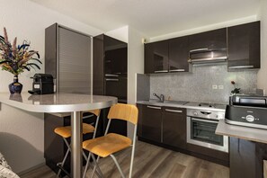 Una cucina moderna con mobili scuri, un piano di lavoro in acciaio inossidabile e un forno integrato. È presente un'area pranzo con un tavolo rotondo e due sedie.