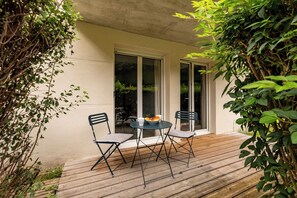 Un patio esterno con due sedie e un tavolo, immerso nel verde e con una parete color crema.