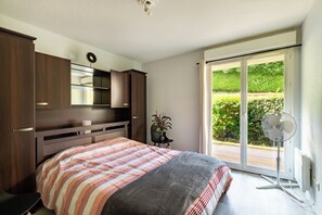 Una camera da letto con un letto, una cassettiera, uno specchio, una pianta in vaso e una porta-finestra su un balcone.