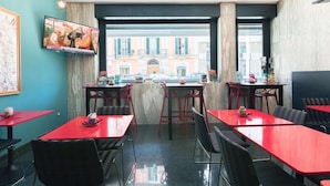 A restaurant with red tables and black chairs, a TV mounted on the wall, and a view of buildings outside. - Hotel Executive Business (Bari)