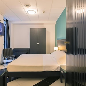 A hotel room with a bed, a desk, a chair, a wardrobe, and a television.