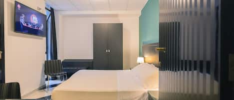 A hotel room with a bed, a desk, a chair, a TV, a wardrobe, and a window with blinds.