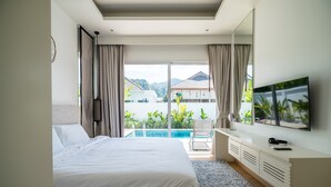 A modern hotel room with a large bed, a TV, and a view of a swimming pool and buildings. - Kamala Garden View villa by Lofty  (Kamala)