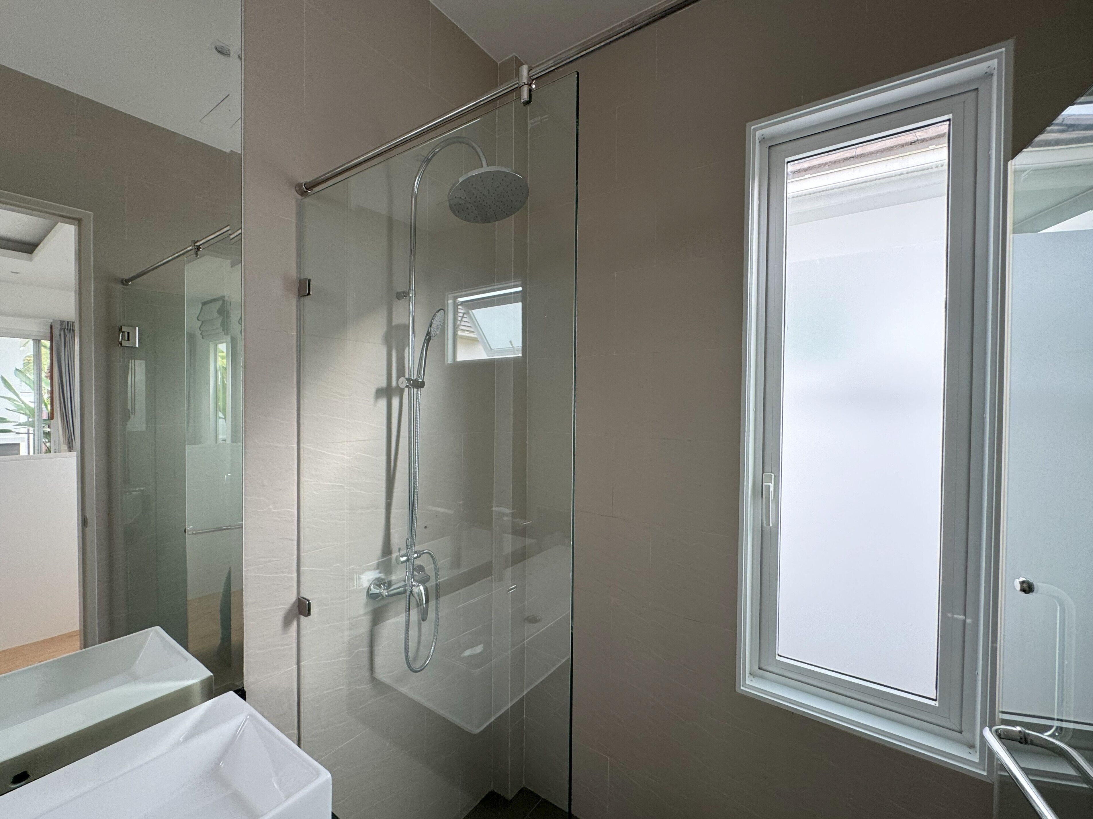 A modern bathroom with a glass-enclosed shower, a white sink, and a window.