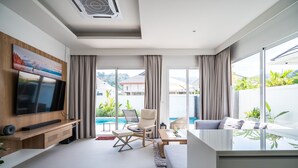 A modern living room with a flat-screen TV, a comfortable seating area, and a view of the outdoors. - Kamala Garden View villa by Lofty  (Kamala)