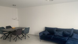 A modern living space with a dark blue sectional sofa, a dining table with chairs, and a pendant light fixture.