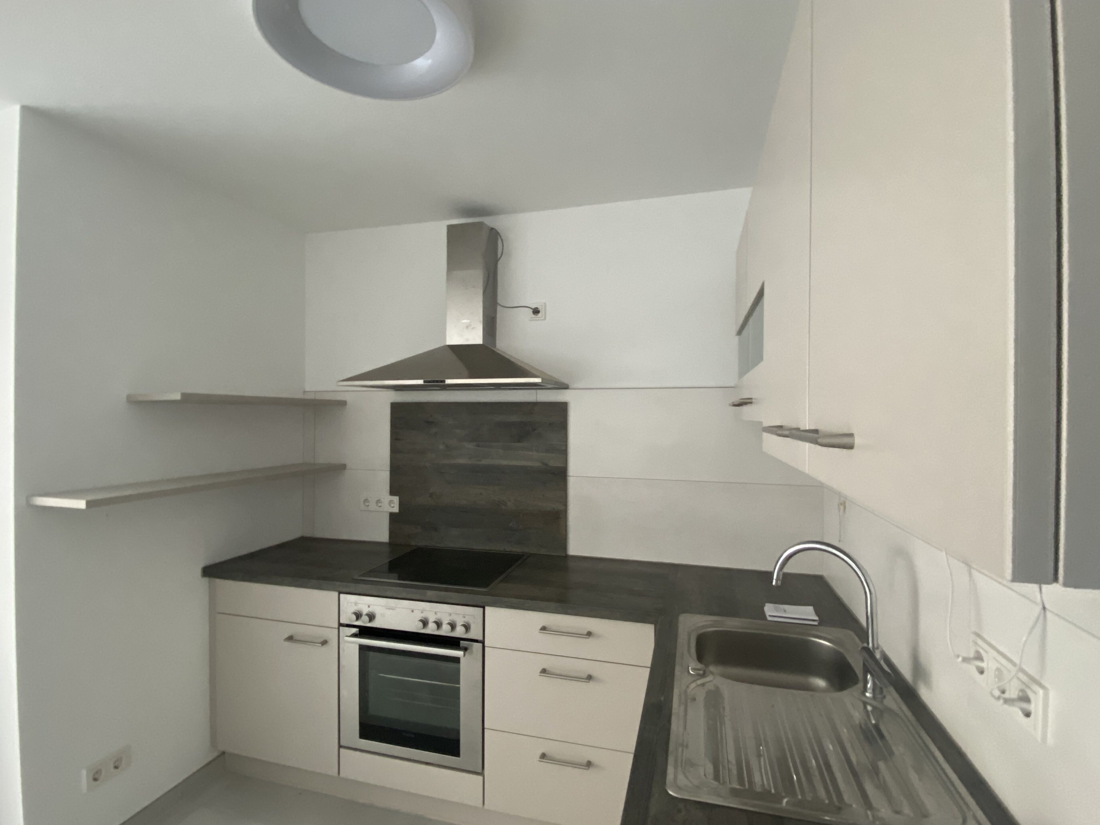 A compact kitchen with a built-in oven, a stainless steel range hood, and a single sink.