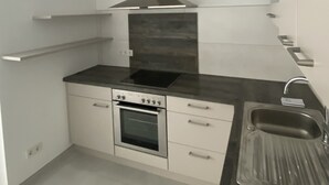 A modern kitchen with a built-in oven, a stovetop, a stainless steel range hood, and a single sink.