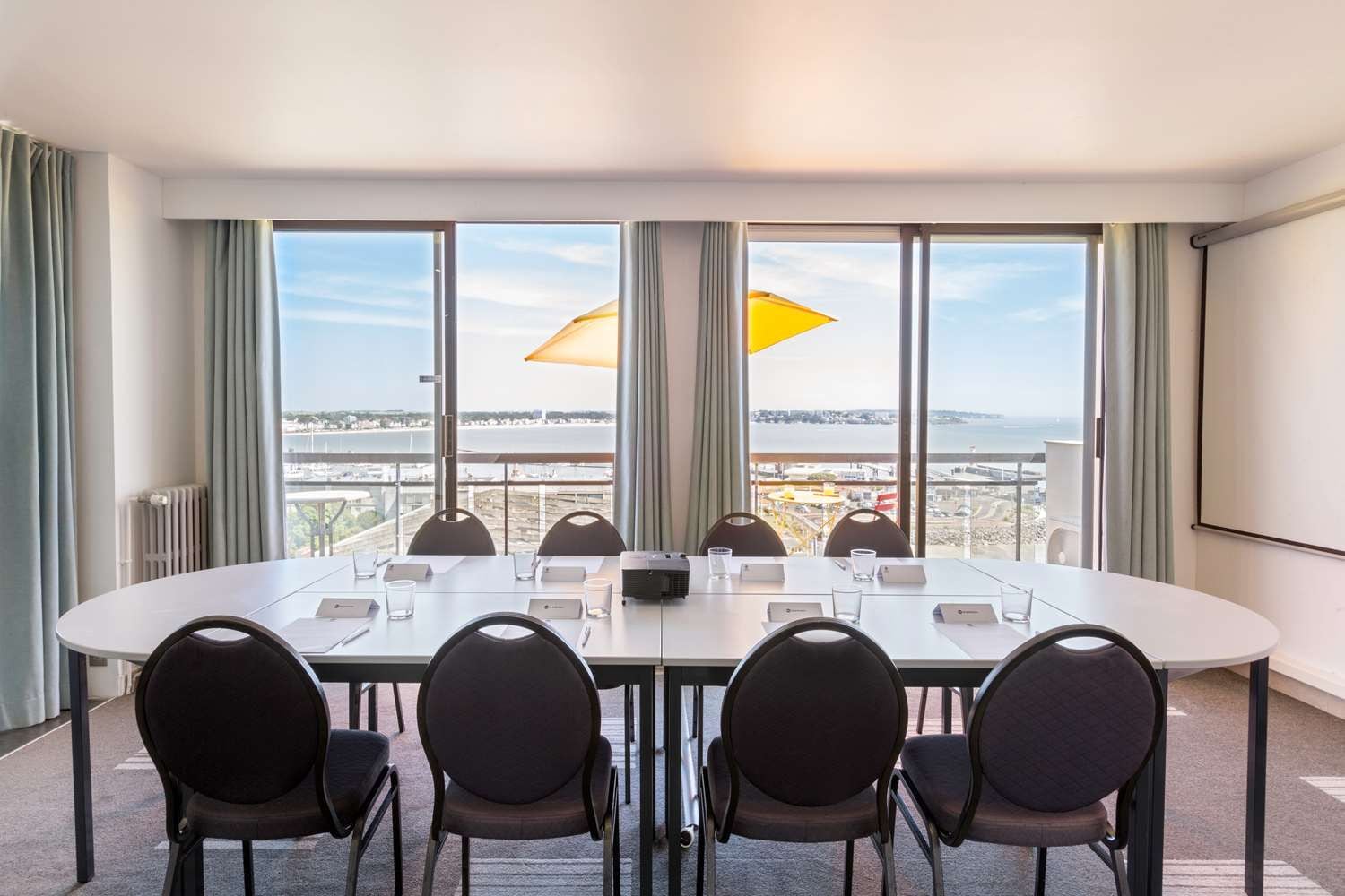 Une salle de conférence équipée d’une grande table, de six chaises, d’un projecteur et offrant une vue sur un pont et sur l’eau.