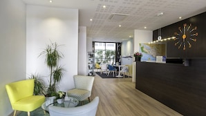 Un hall d’entrée moderne avec une grande horloge murale, un espace détente comprenant des fauteuils, une table basse et une plante en pot.