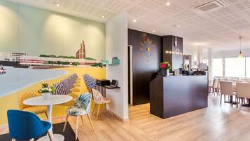 Un lobby moderno de hotel con mostrador de recepción, zona de estar y un mural de un paisaje urbano.