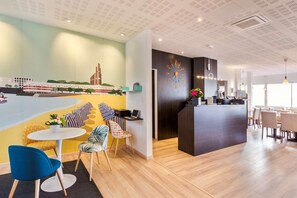 Eine moderne Hotelhalle mit einer Rezeption, einer Sitzecke und einem Wandbild einer Stadtansicht.