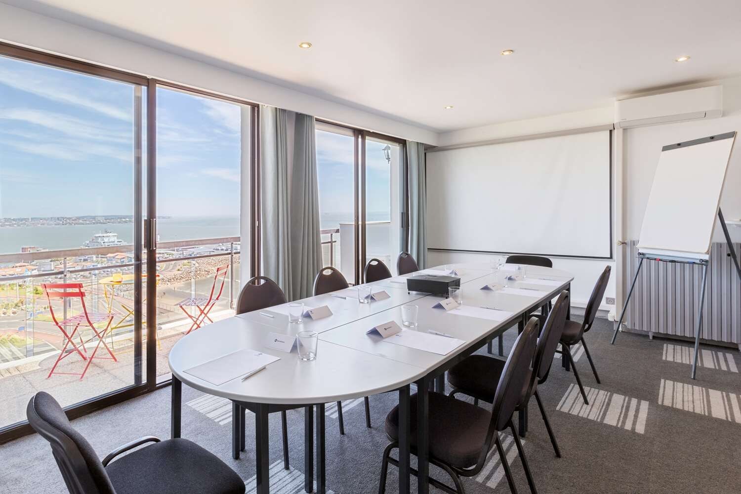 Un salón de conferencias con una gran mesa, sillas, una pizarra y vistas a una masa de agua a través de amplias ventanas.