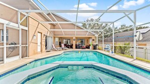 Una piscina con una estructura de sombrilla, una canasta de baloncesto y un área de descanso con sillas y una mesa.