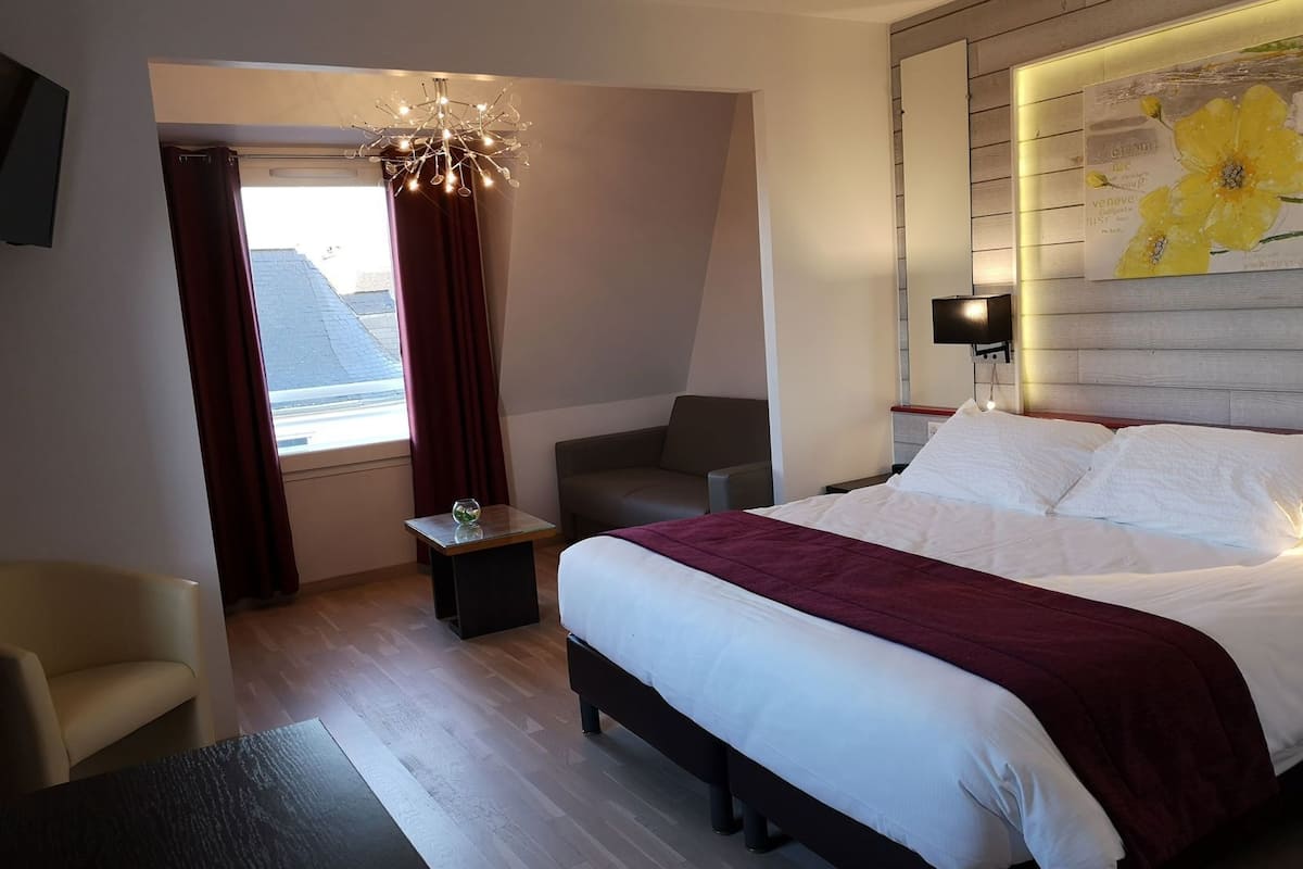A modern hotel room with a bed, a desk, a chair, a window with curtains, and a wall-mounted TV.