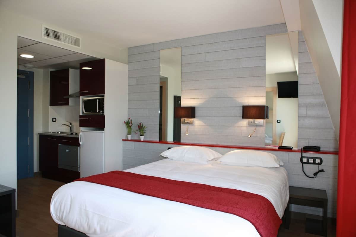 A hotel room with a bed, a desk, a microwave, and a small kitchenette.