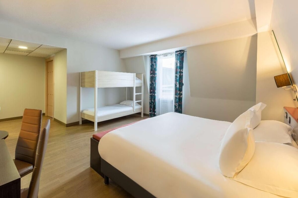 Habitación de hotel con literas, una cama individual, un escritorio con silla y ventana con cortinas.