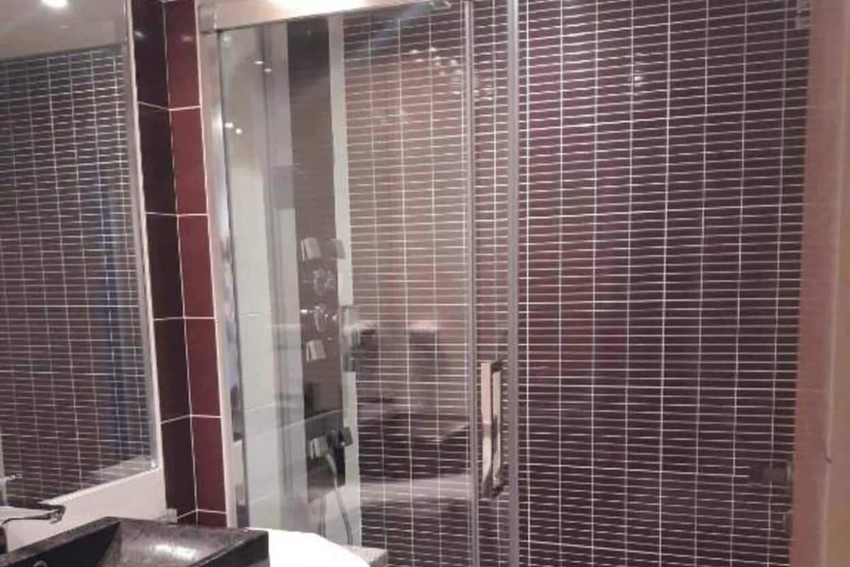 A modern bathroom with a glass shower enclosure, a granite countertop, and a large mirror.