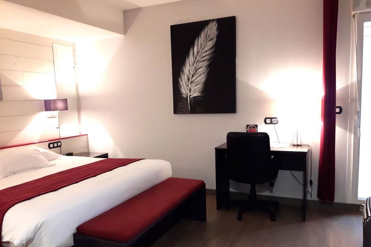 A hotel room with a bed, desk, chair, and a feather artwork on the wall.