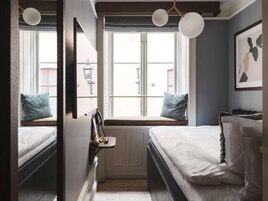 Un dormitorio con dos camas, un asiento junto a la ventana con una lámpara y un cuadro en la pared.