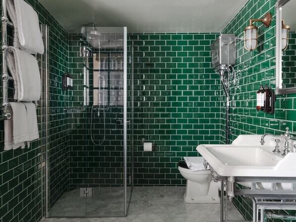 A bathroom with green tiled walls, a glass shower enclosure, a white sink, and a toilet. - Best Western Plus Hotel Frantz (Stockholm)
