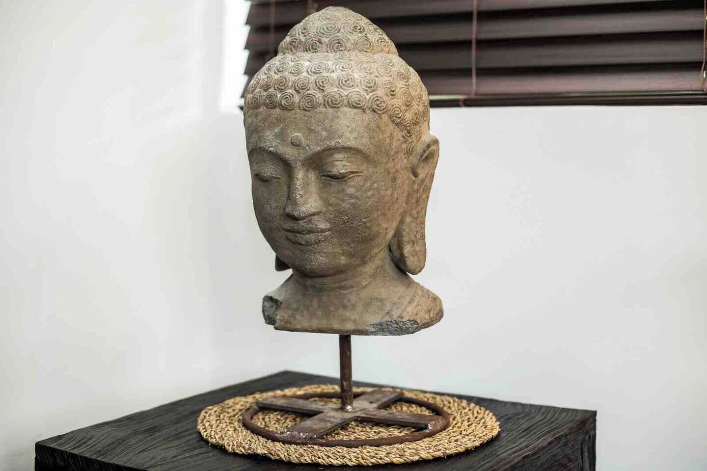 Una escultura de cabeza de Buda de piedra sobre un pedestal con una base tejida.