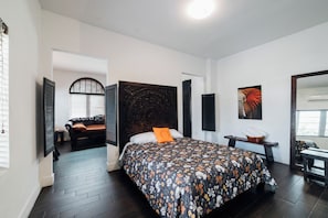 A bedroom with a large bed, a headboard, a nightstand, a window, and a door leading to another room.