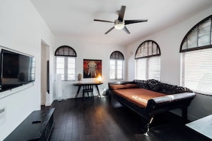 A room with a bed, a desk, a television, and a ceiling fan.